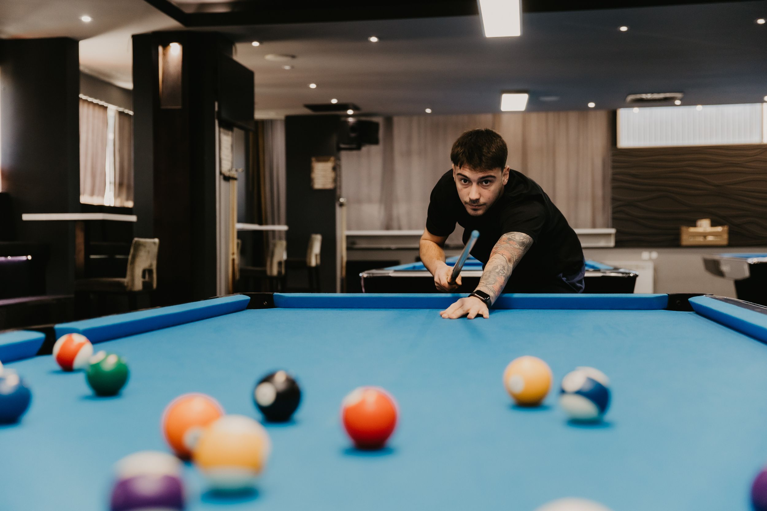 Pool player lining up a shot on a blue felt billiards table with scattered colorful balls.