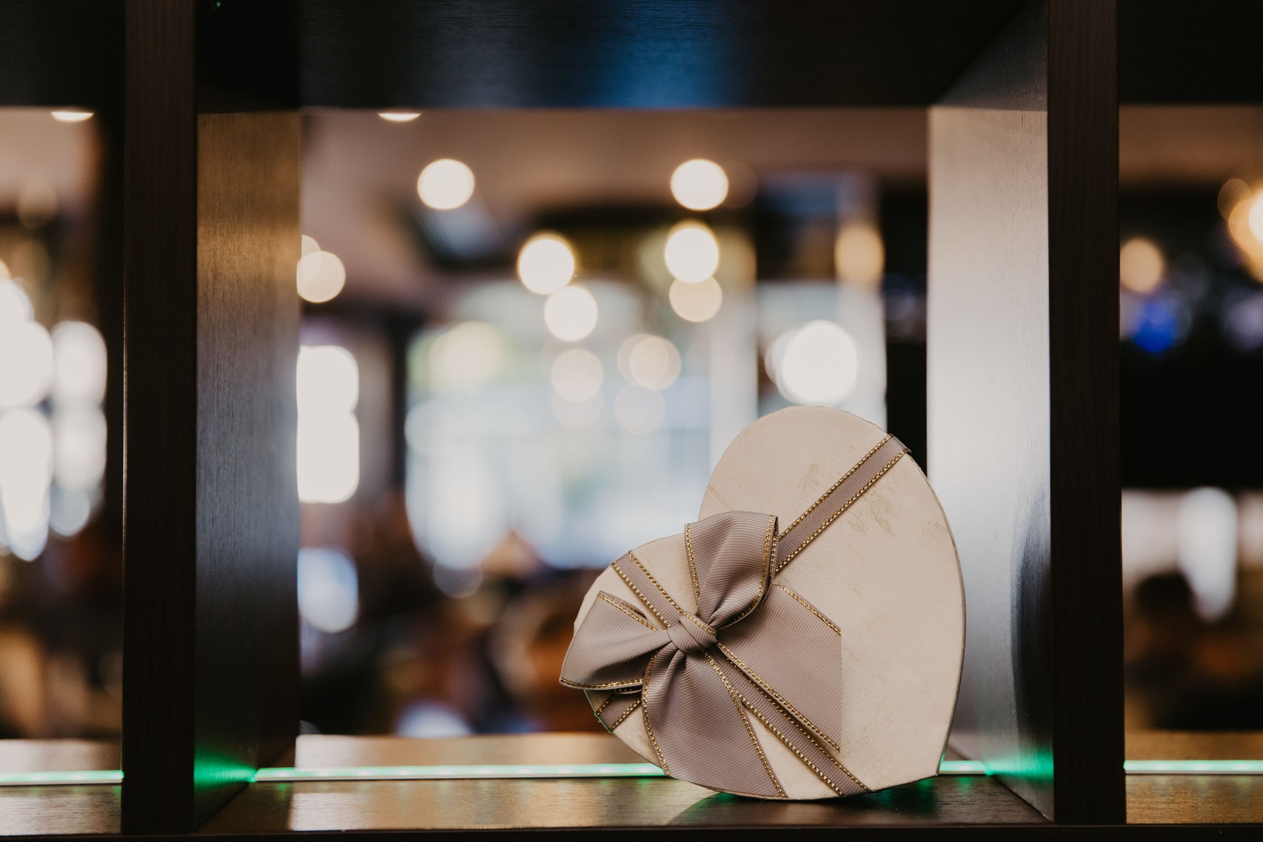 Elegant heart-shaped gift box with bow displayed on glass shelf with bokeh background.