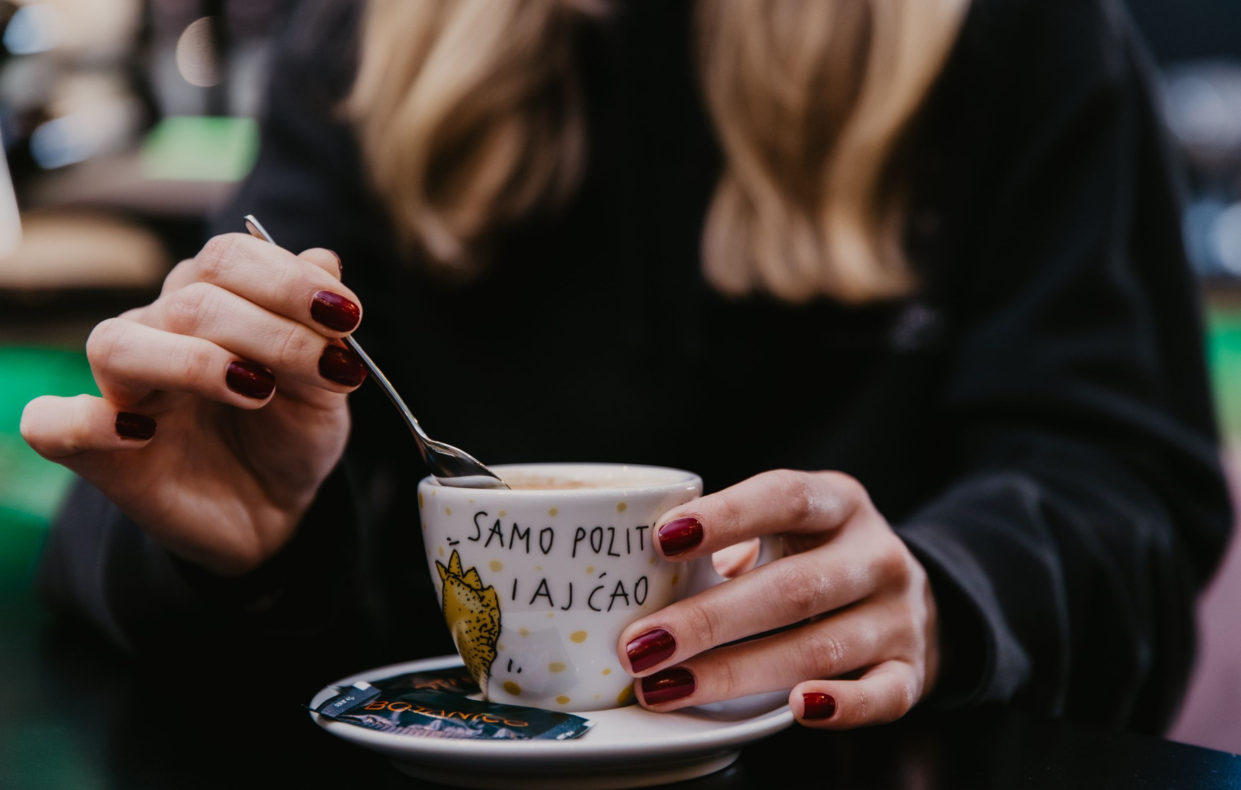 Hands holding decorated coffee cup and saucer against blurred cafe background.