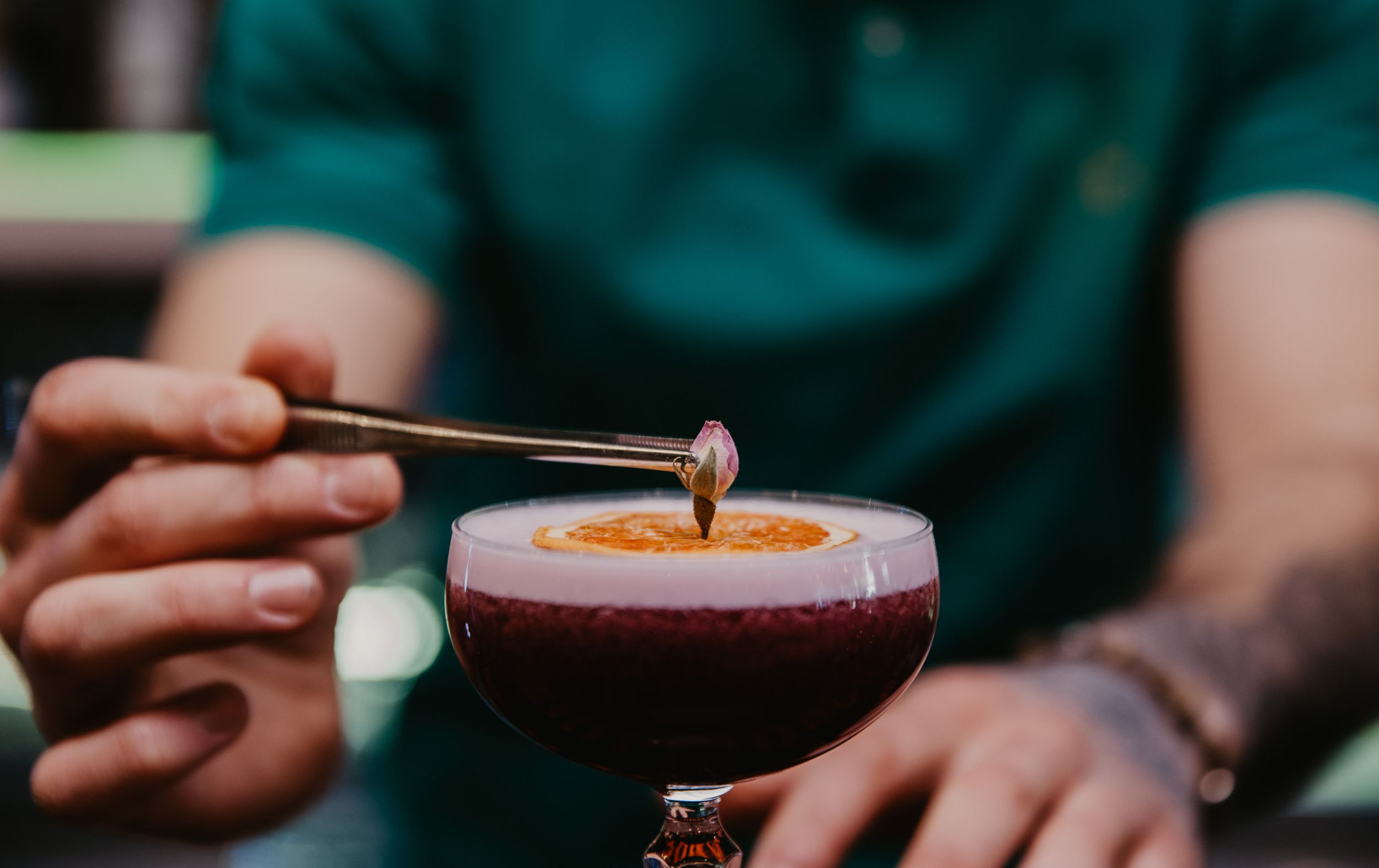 Close-up of garnishing a dark cocktail with dropper at bar counter.
