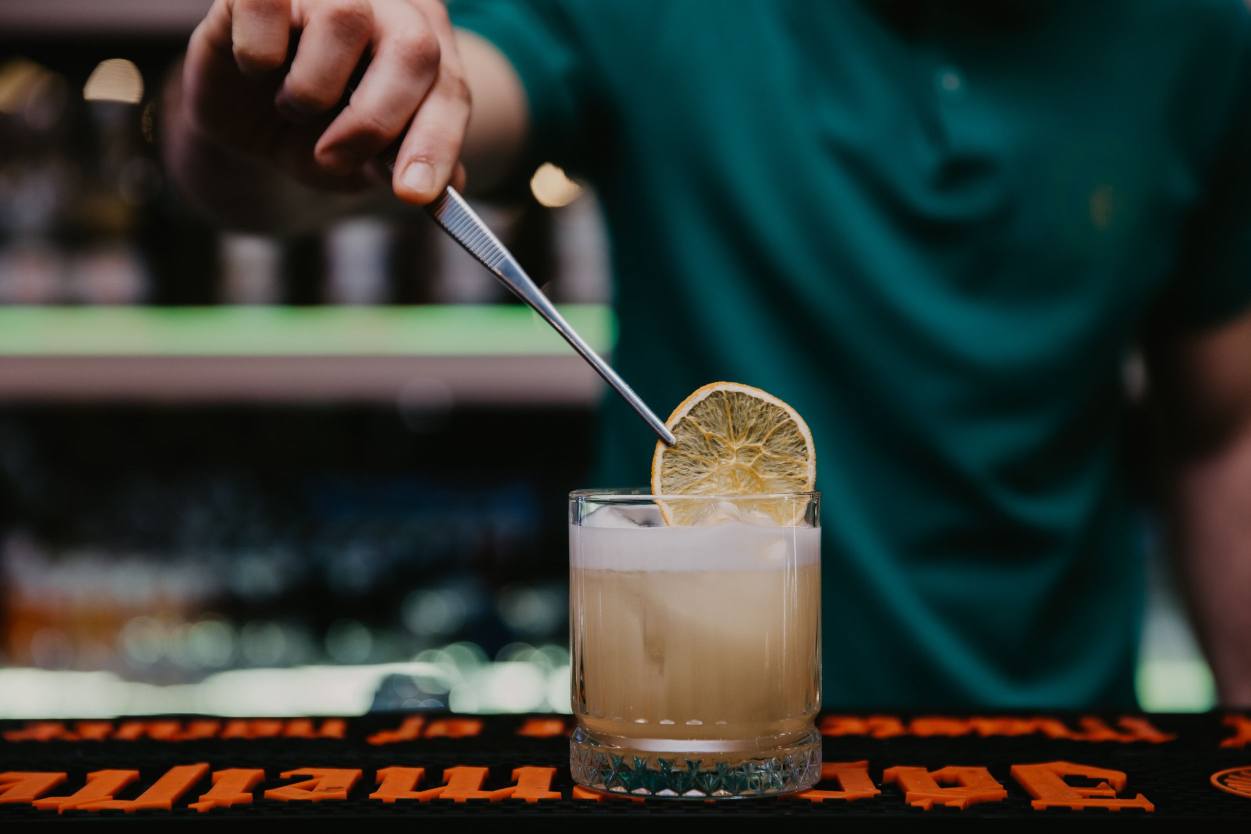Bartender adding citrus garnish to light-colored cocktail at bar counter.