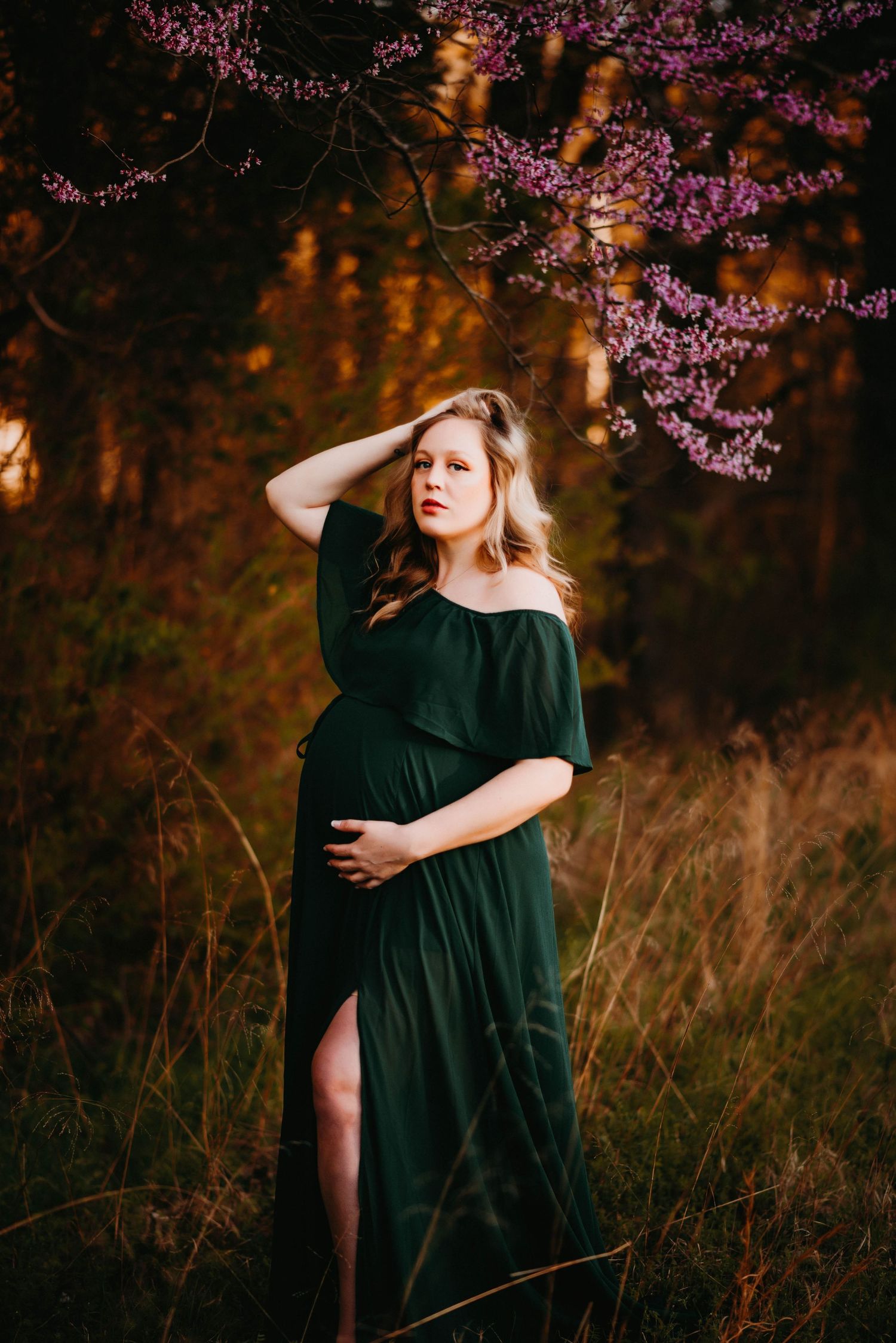 Romantic maternity photos under blooming cherry blossoms wearing an elegant green velvet dress.