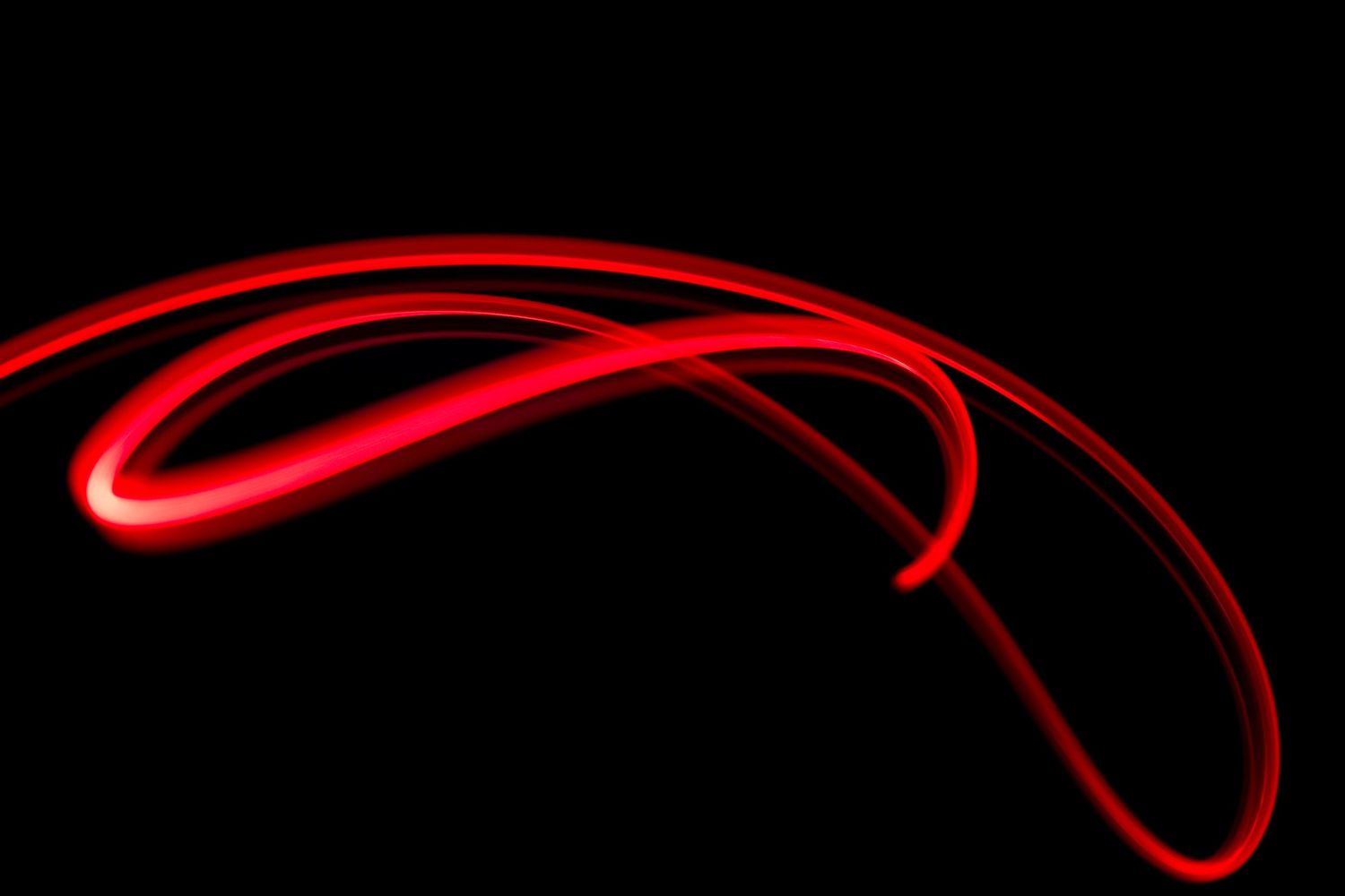 Abstract red light trails creating curved patterns against black background.