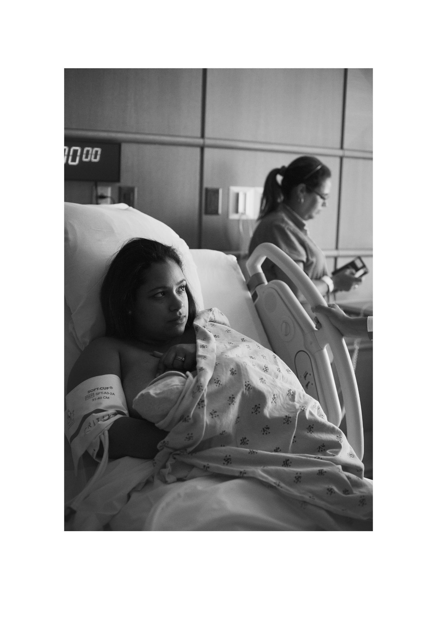Black and white photo of a young mother holding her newborn in a hospital bed after delivery.