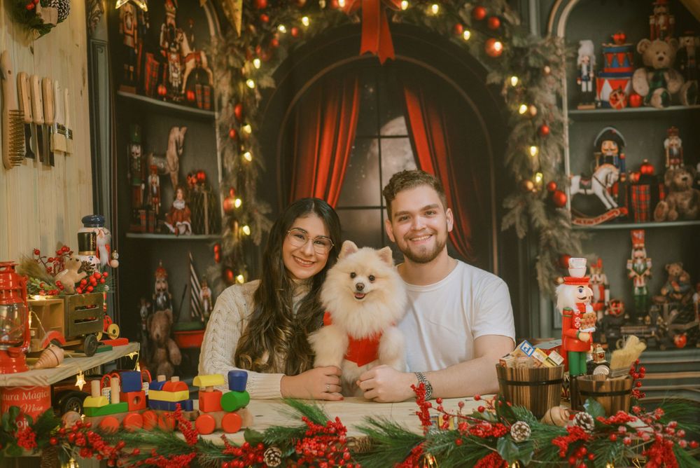 Cozy Christmas scene with couple and white Pomeranian dog surrounded by holiday decorations and lights.