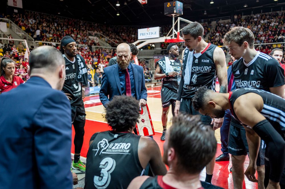 Basketball team huddle during timeout with coaches and players on court.
