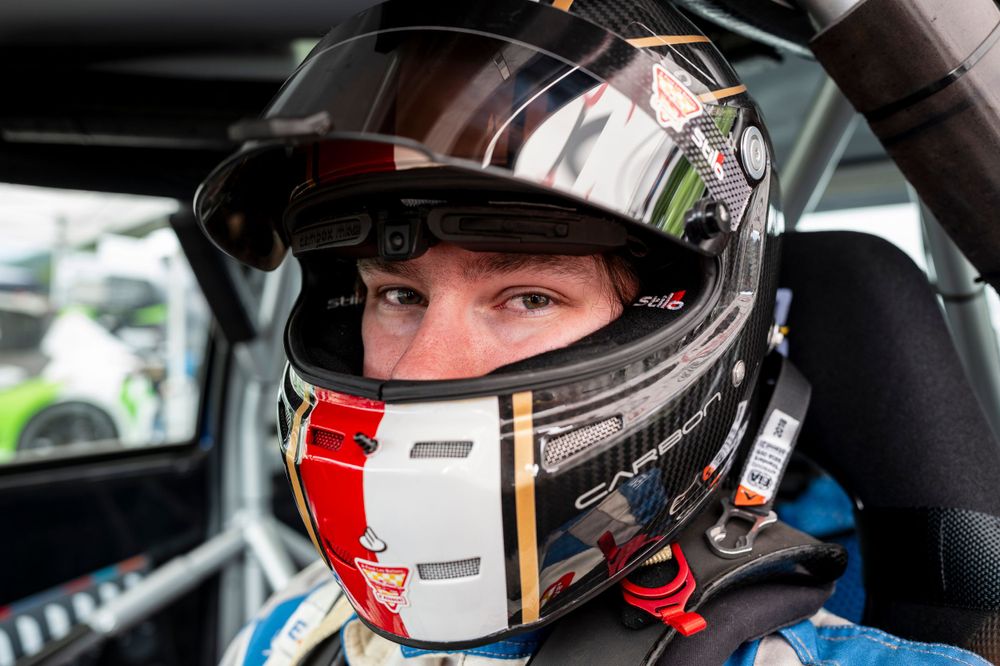 Race car driver wearing striped helmet inside vehicle cockpit.