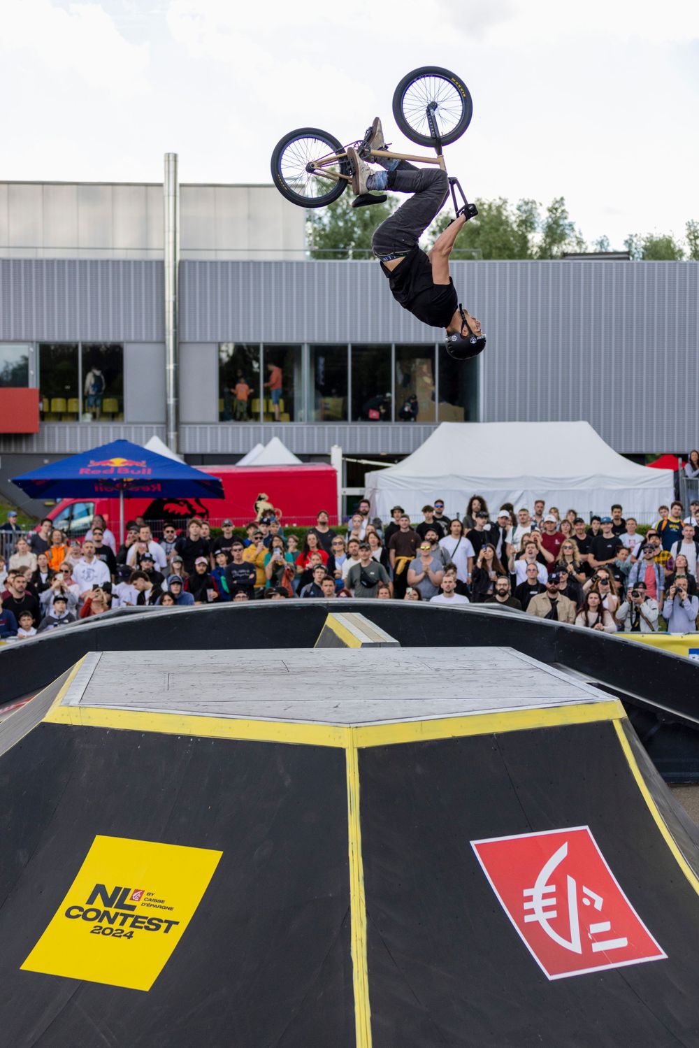 BMX rider performing an impressive backflip trick over a ramp at an outdoor competition.