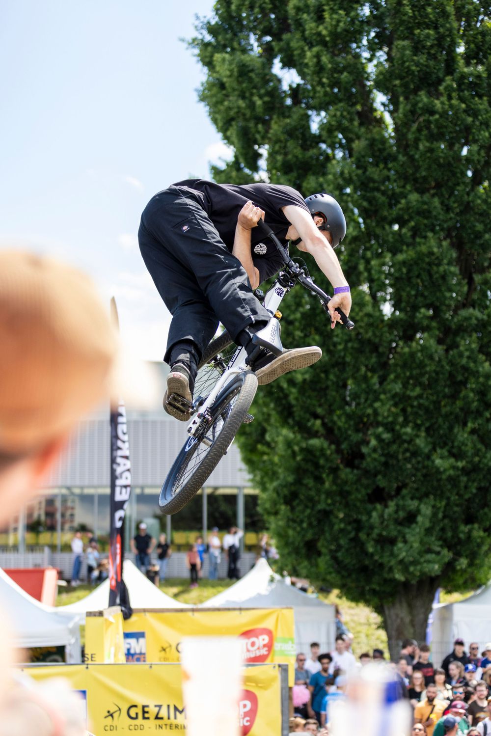 BMX rider performing aerial tricks during outdoor competition with crowd watching below.