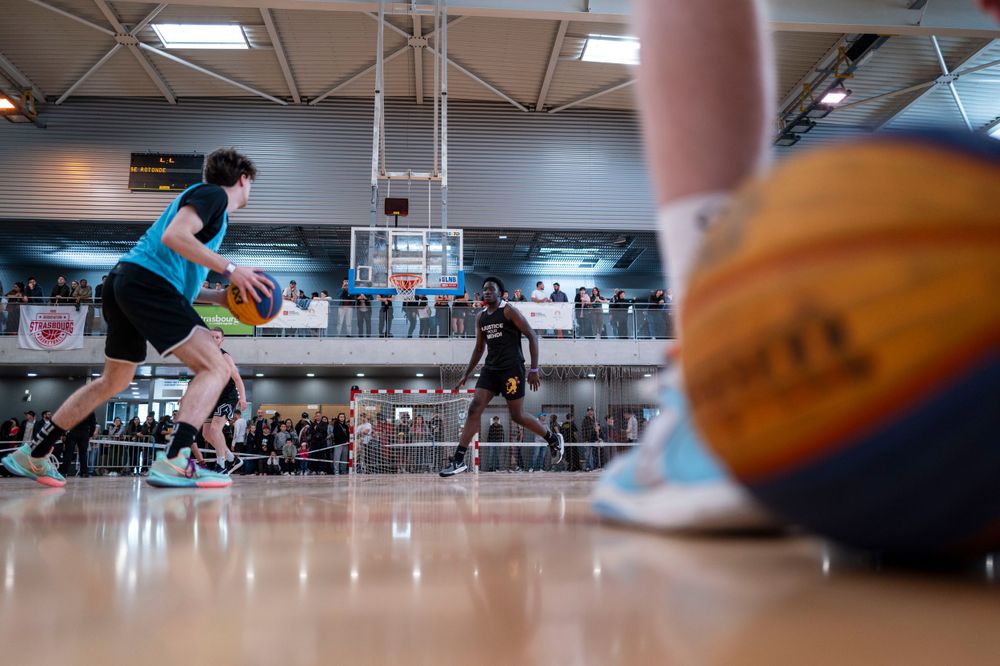 Basketball players in action on indoor court with ball visible in foreground.