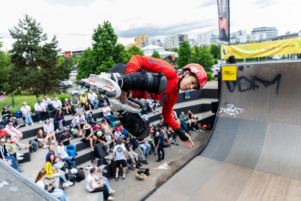 Athlete in red performing aerial stunt on skateboard ramp with crowd watching below.