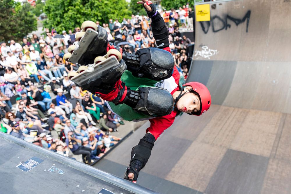 Skater performing an inverted aerial trick on a half-pipe with spectators in background.