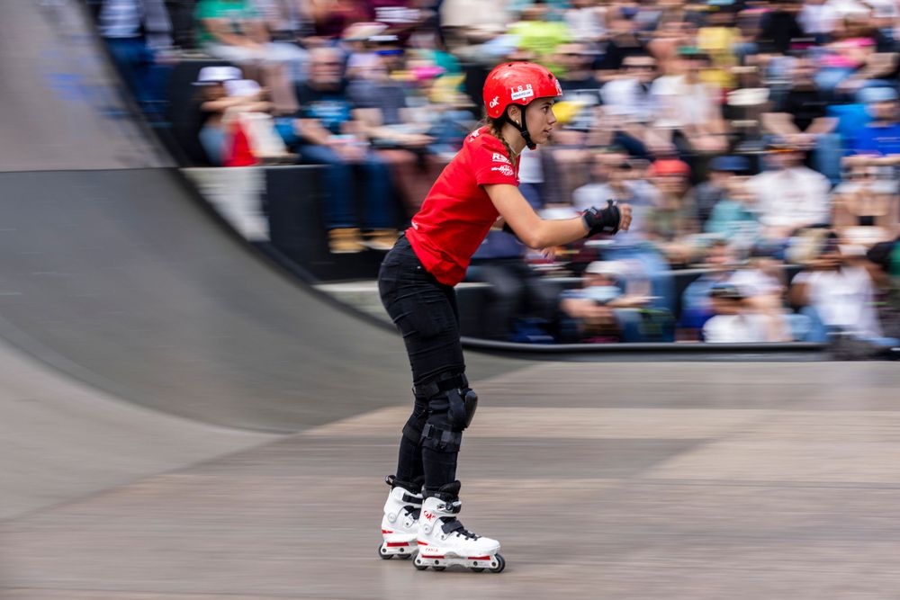 Motion blur of inline skater in red performing on curved ramp at competition.