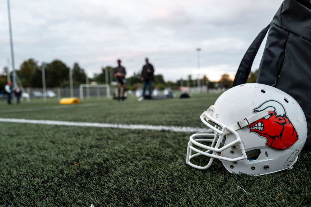 White football helmet with red logo rests on grass field during practice.