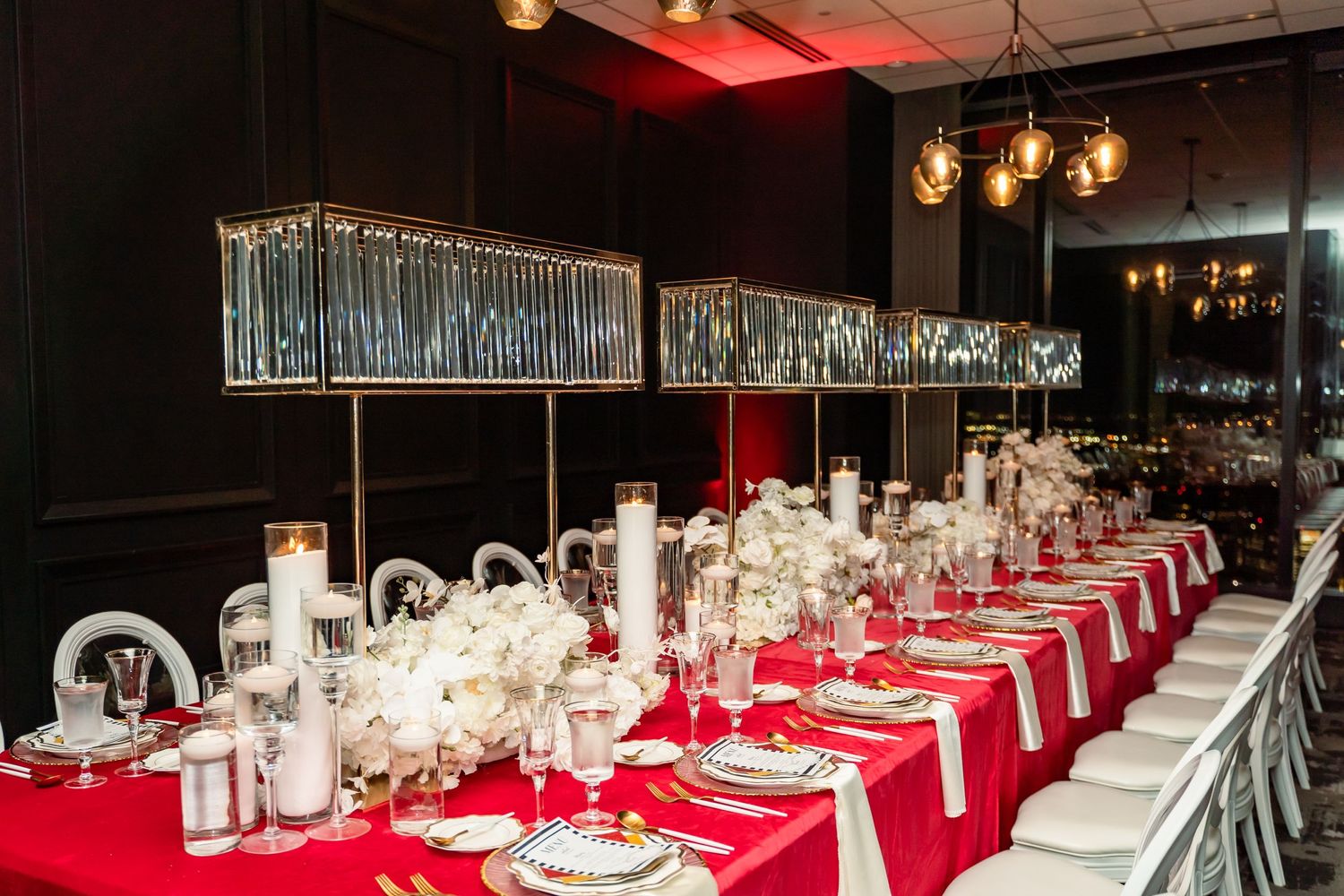 Elegant table setting with red runner and crystal chandeliers in dark dining room.