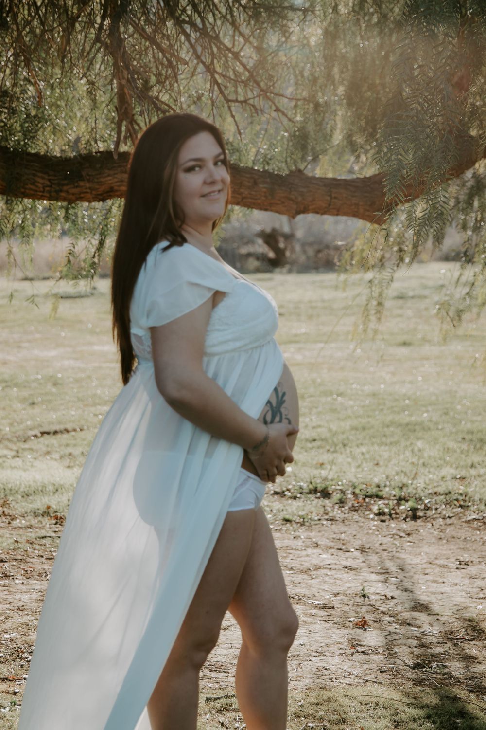 Dreamy maternity portrait under willow trees in a flowy white dress.