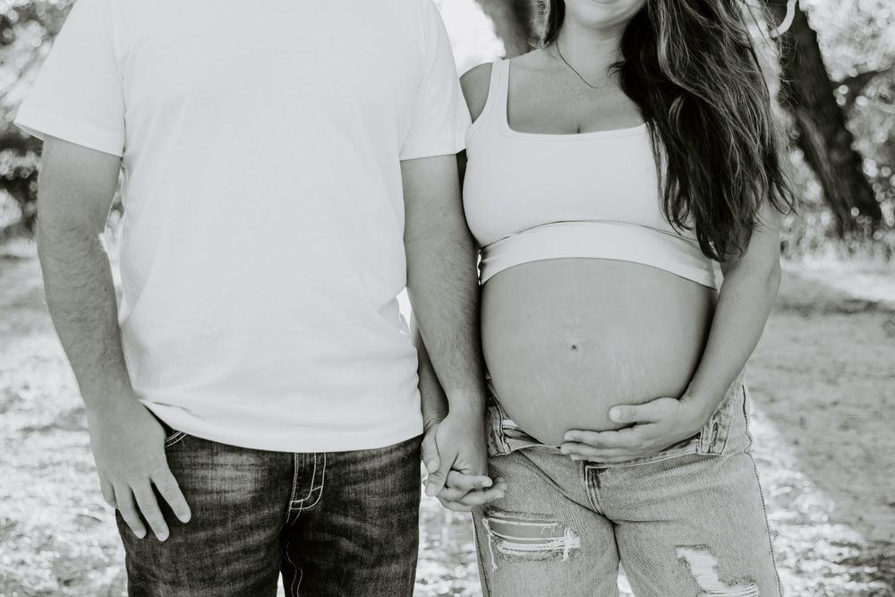 A black and white maternity photo showing couple's torsos in casual attire.