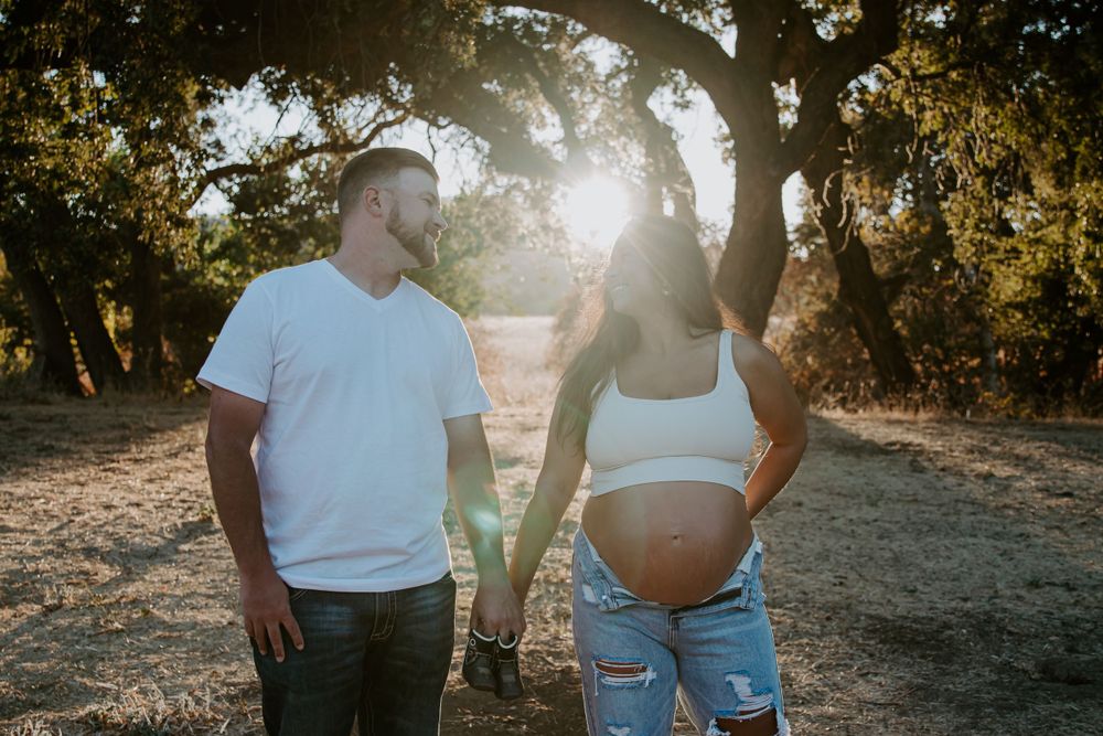 A maternity photo shoot at sunset with sun flare through trees.