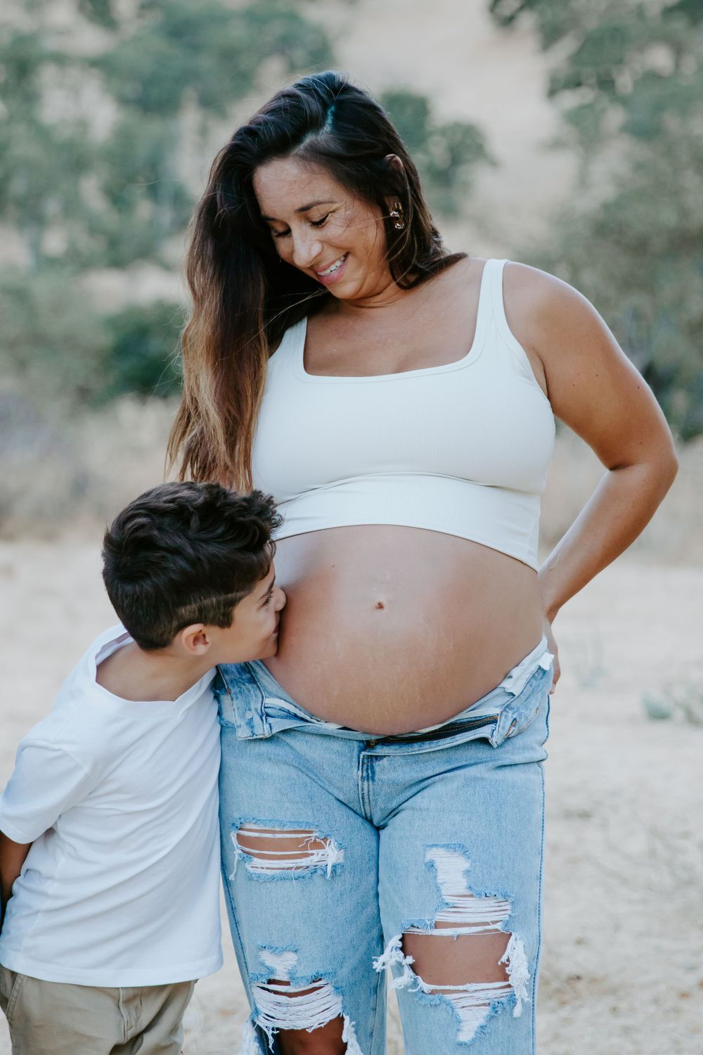 A tender maternity moment captured outdoors in natural lighting.