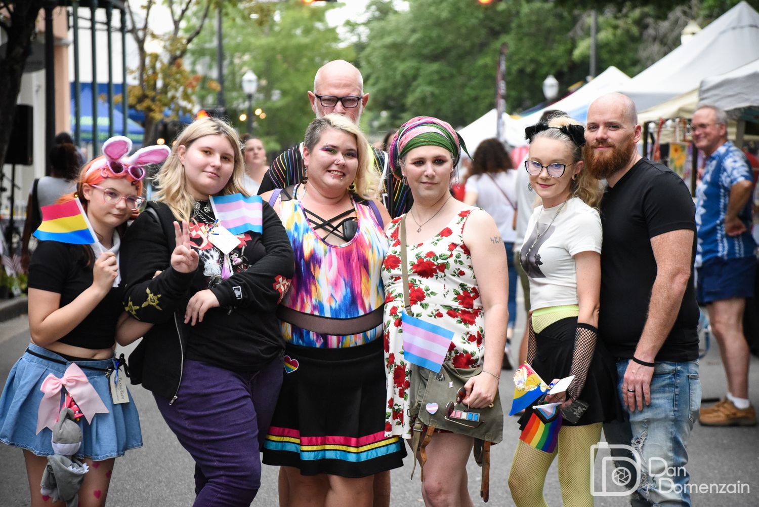A colorful group gathering at an outdoor pride festival with vibrant attire and decorations.