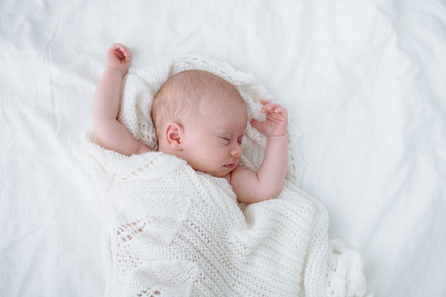 Sleeping newborn baby in knit sweater being held horizontally against white background.