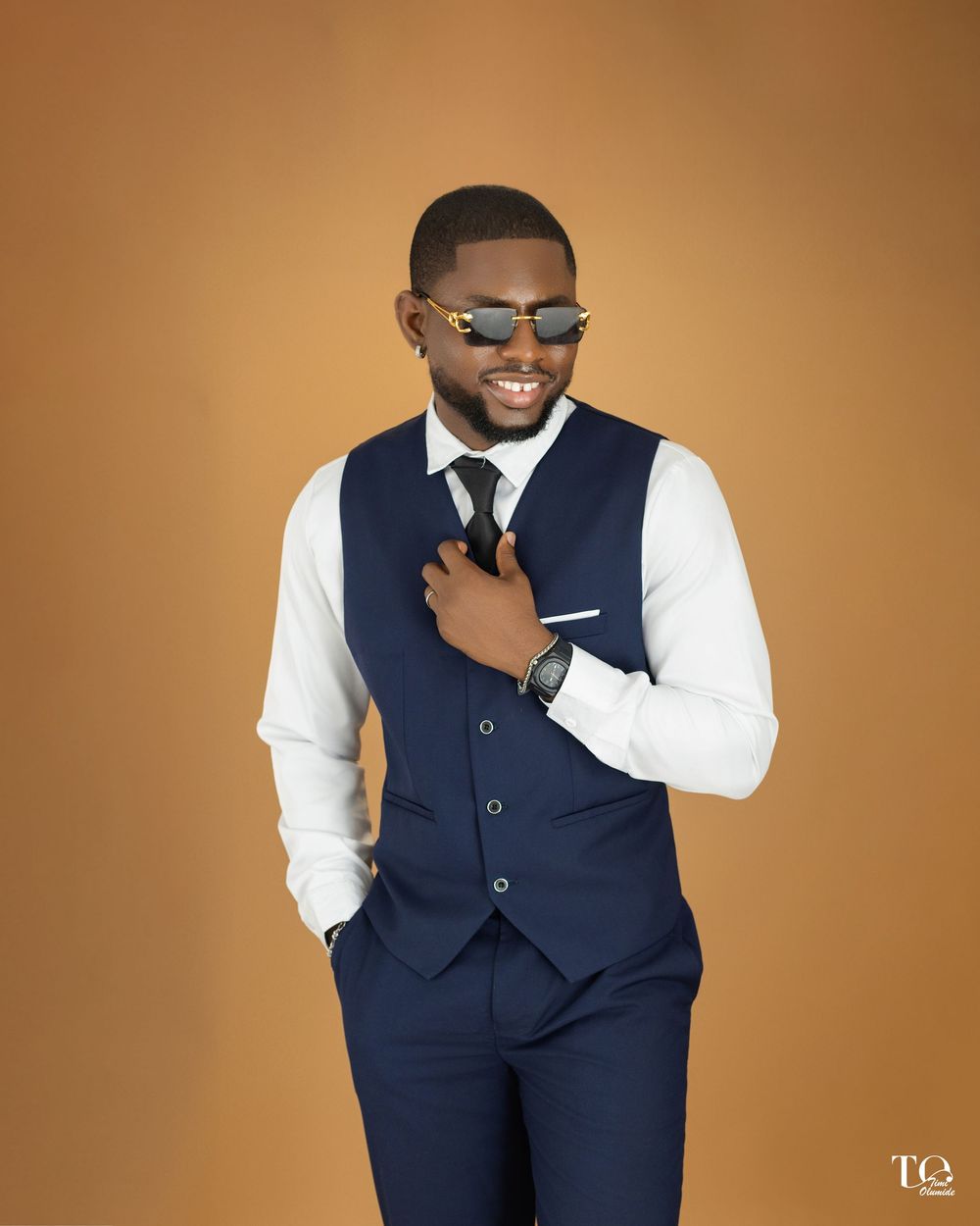 Stylish man in navy vest and white dress shirt poses confidently against brown backdrop in professional photoshoot.