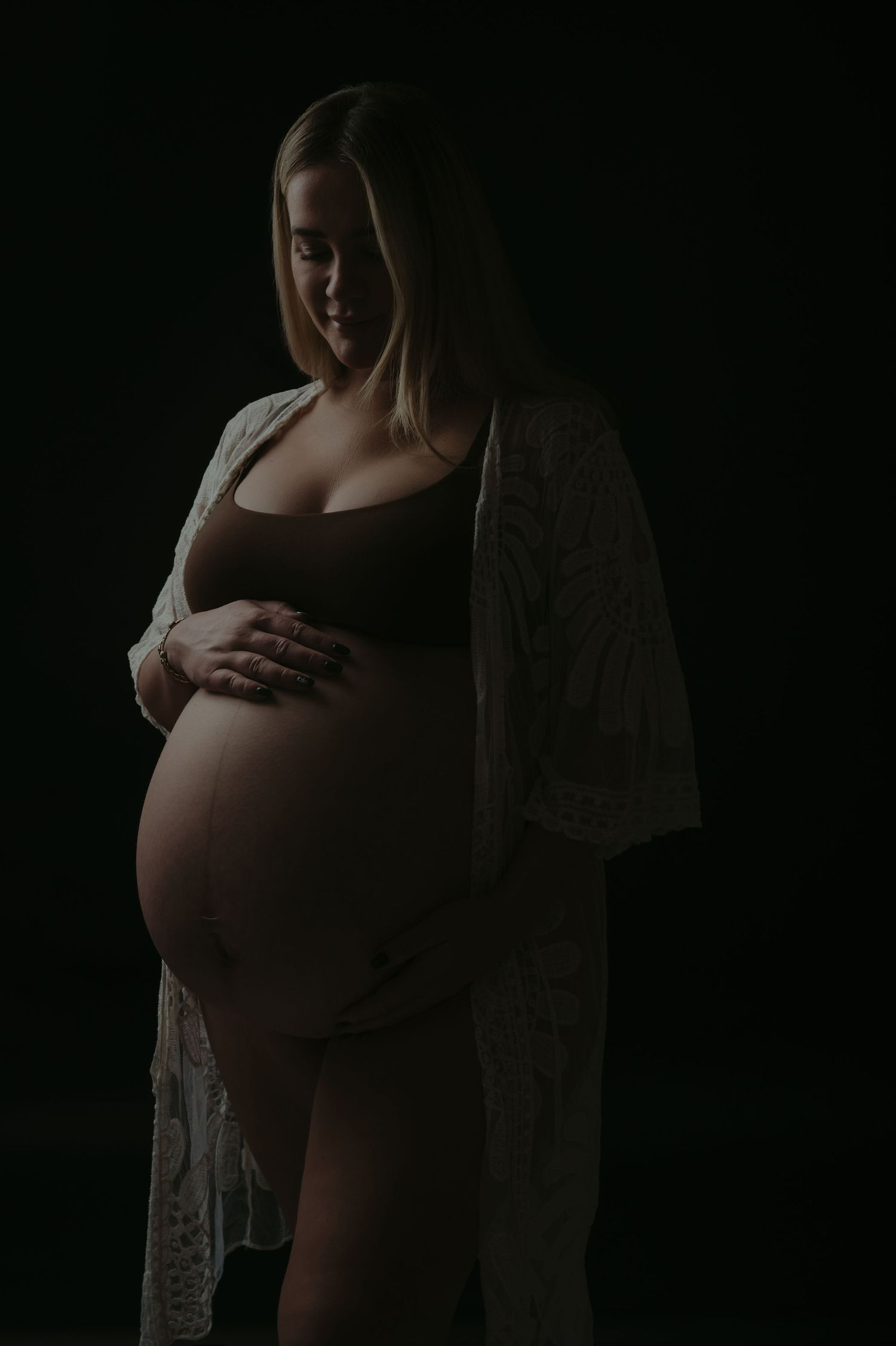 Dramatic black and white silhouette of pregnant woman in profile against dark background.