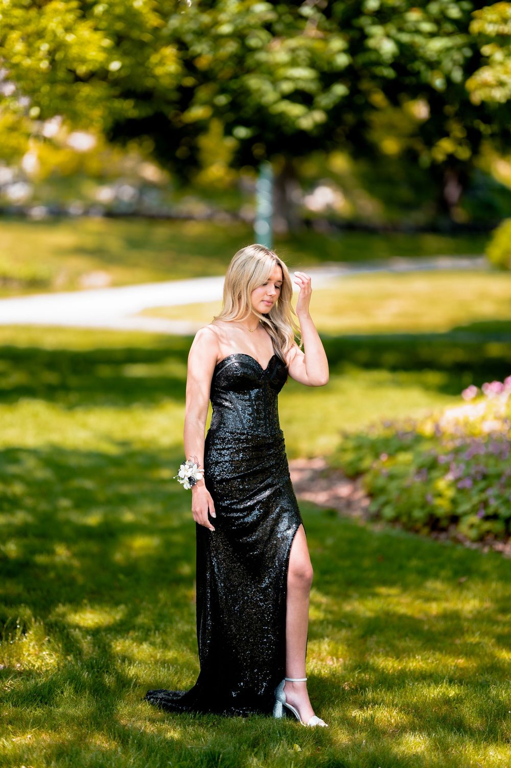 Elegant formal portrait of woman in black sequined gown outdoors in sunlit garden.