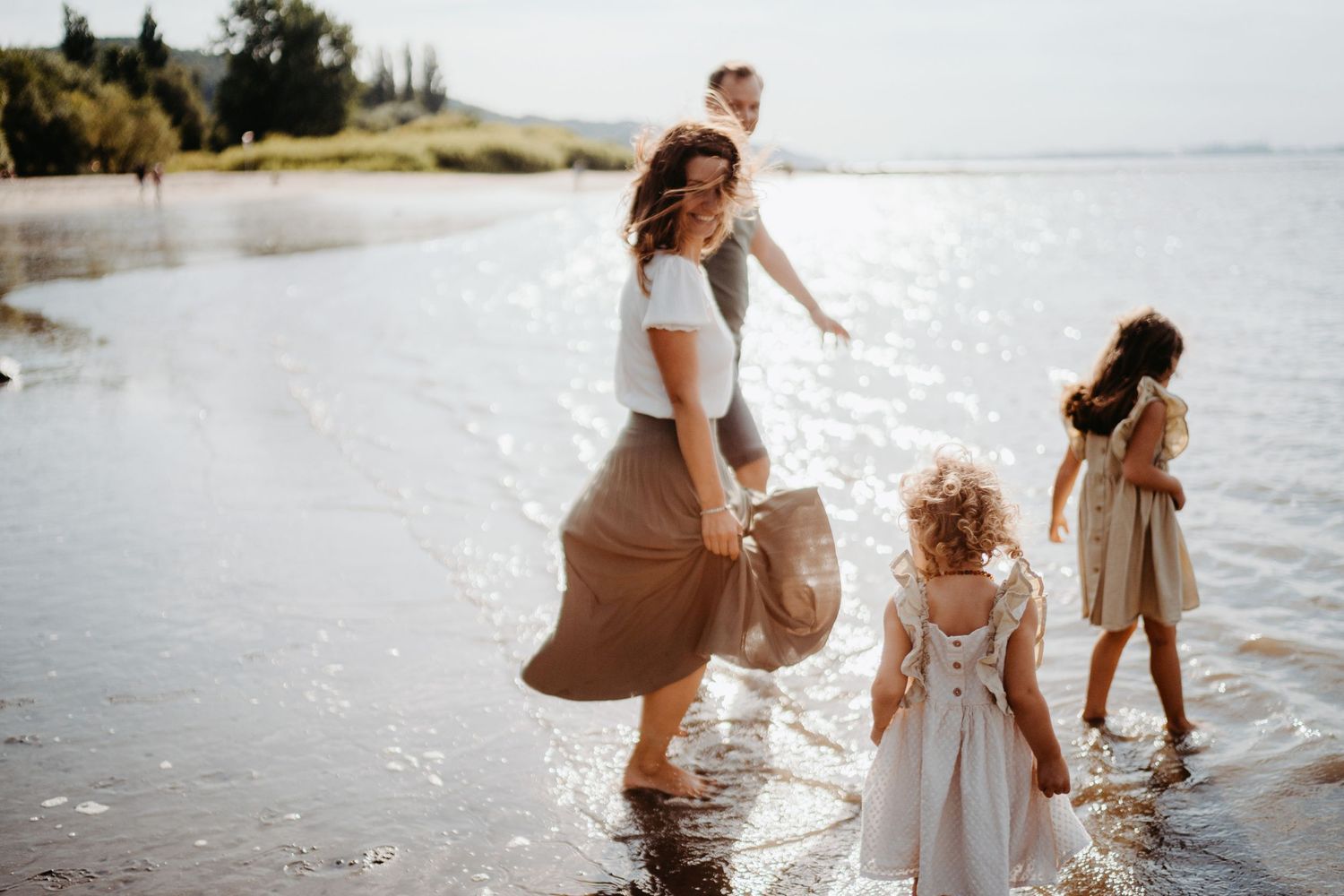 People enjoying a sunny afternoon wading and playing together in sparkling waters along a peaceful beach shoreline.