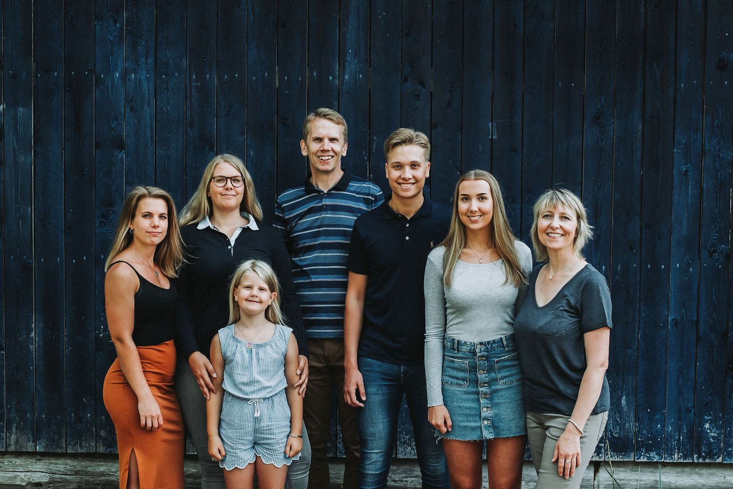 A casual family group portrait against a dark blue wooden wall background.
