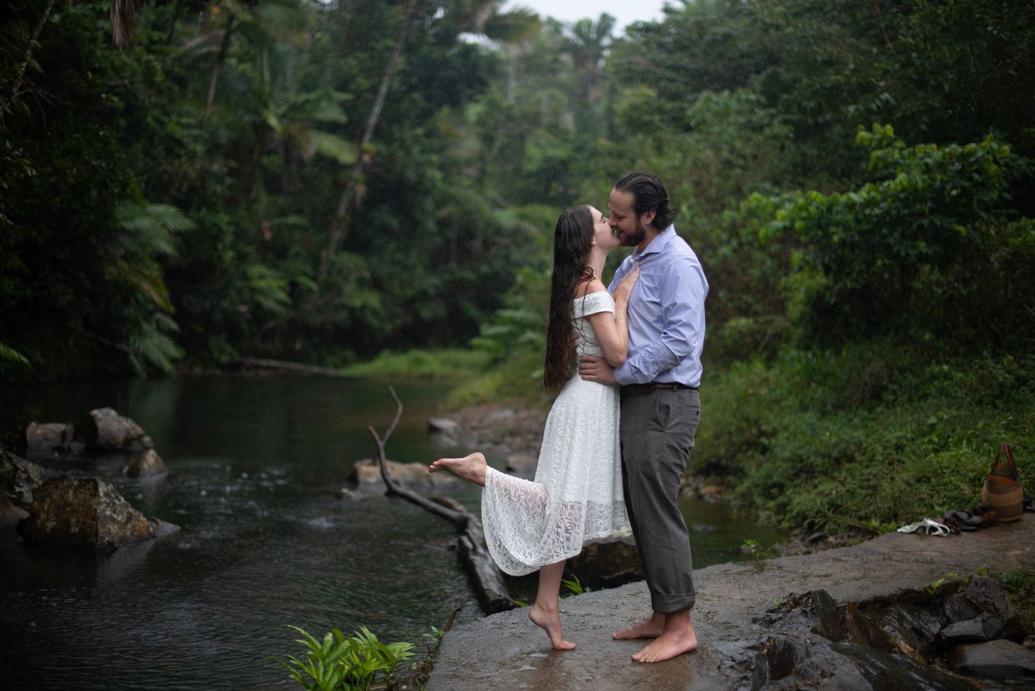 Romantic couple embracing by scenic river surrounded by lush forest.