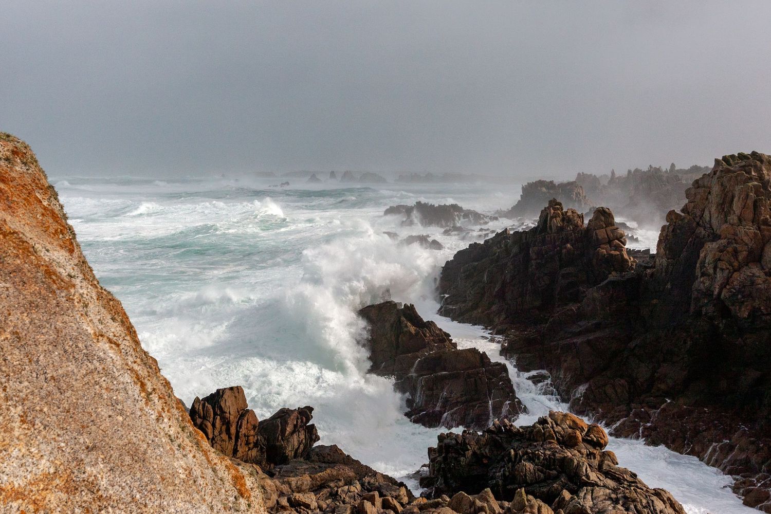 Dramatic waves crash against jagged coastal rocks during stormy weather.