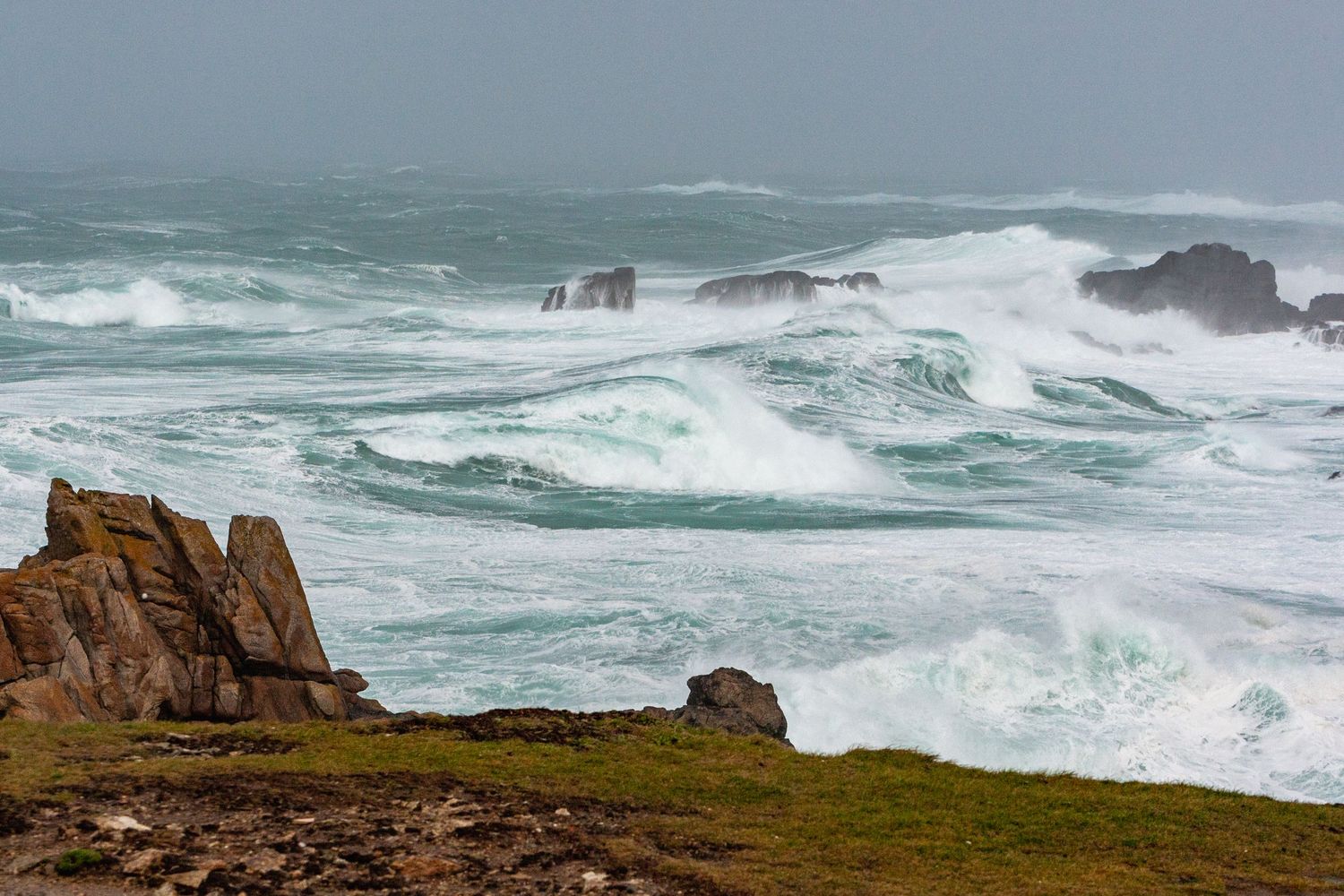 Massive waves break over rocky cliffs along a dramatic stormy coastline.
