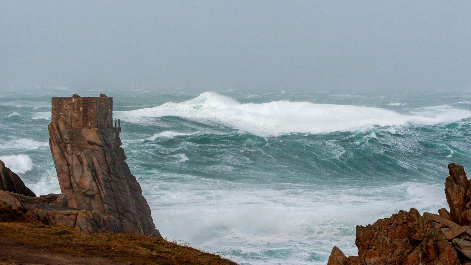 Large waves crash against steep rocky cliffs during coastal storm.