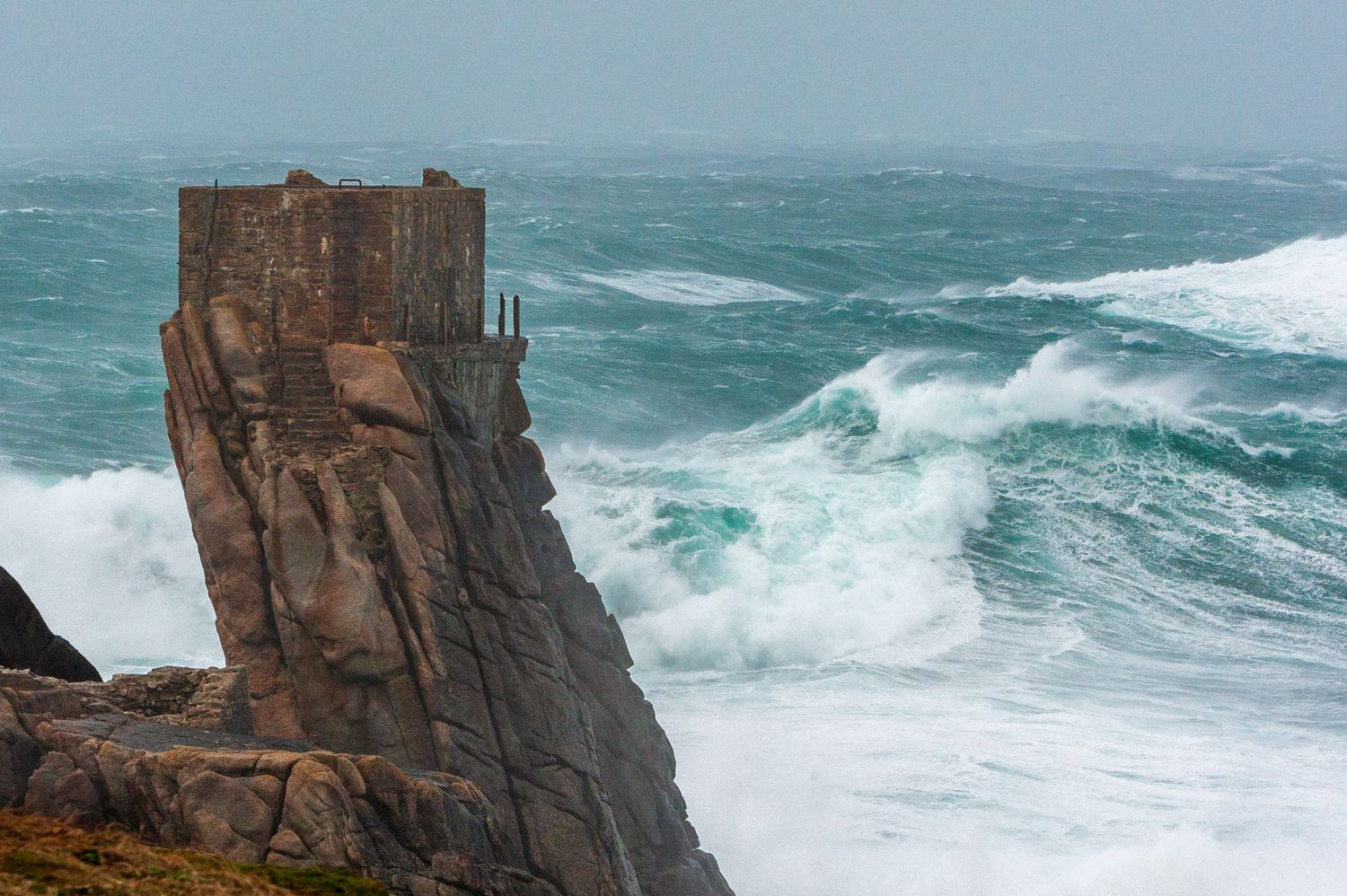 Towering granite cliff formation stands against turbulent ocean waves.