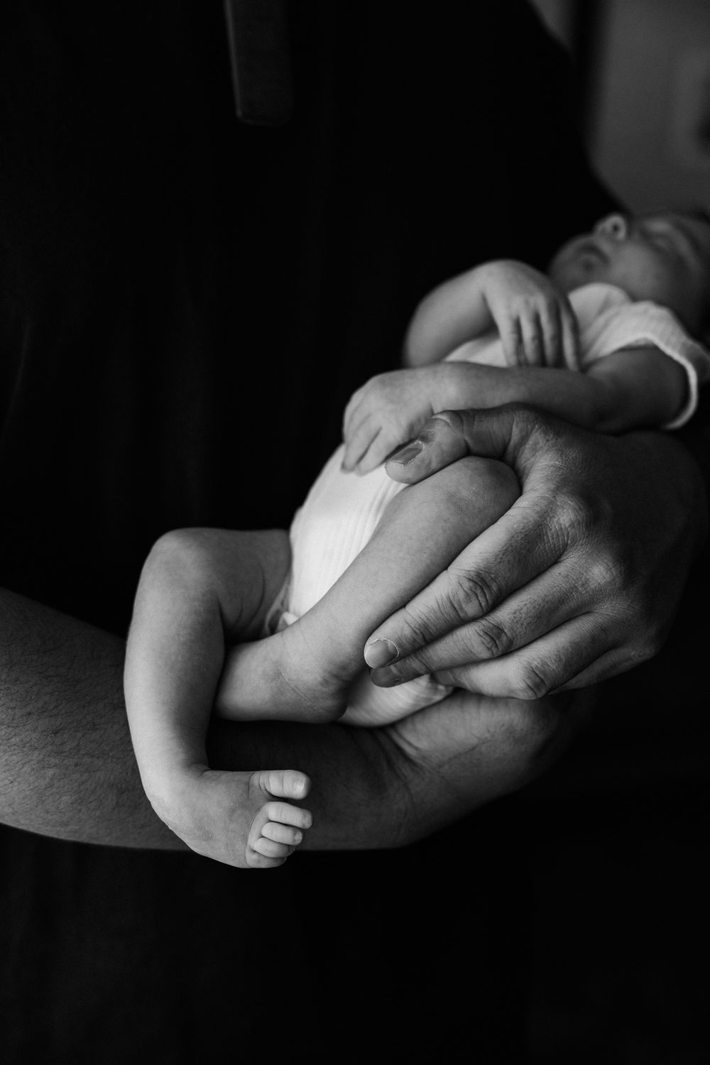 A tender black and white photograph of adult hands gently holding tiny baby feet.