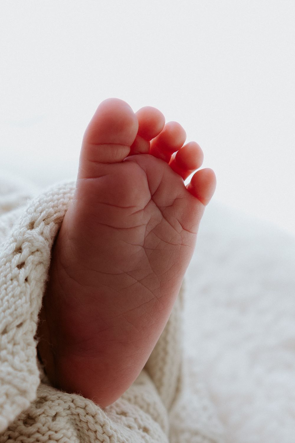 Close-up view of a tiny baby foot wrapped in a soft knit blanket against a light background.