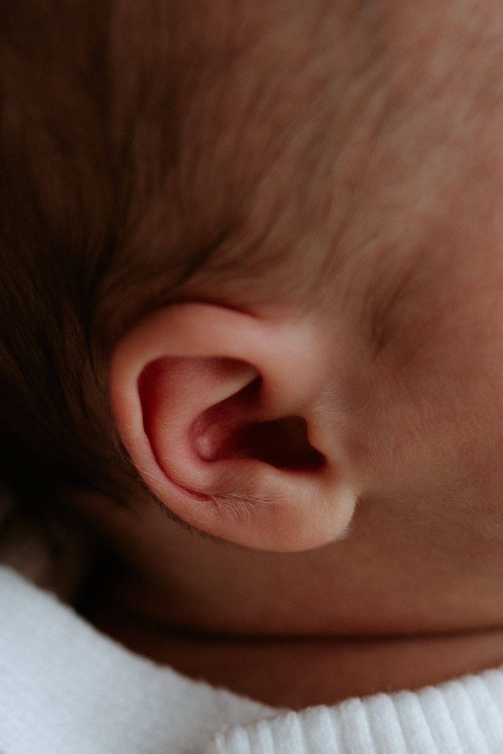 Close-up macro photography of a baby's ear showing delicate details of the outer ear against a soft blurred background.