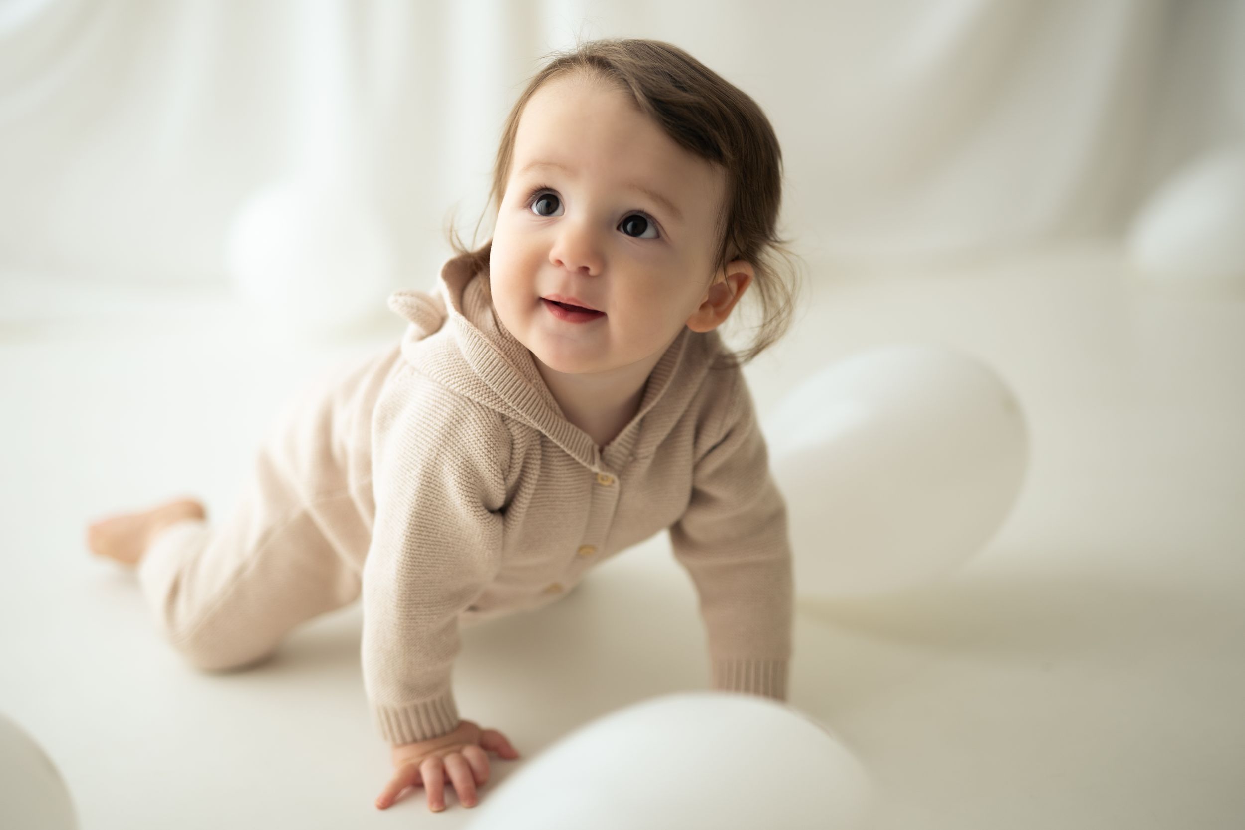 Bambina di un anno gattona in mezzo ai palloncini bianchi