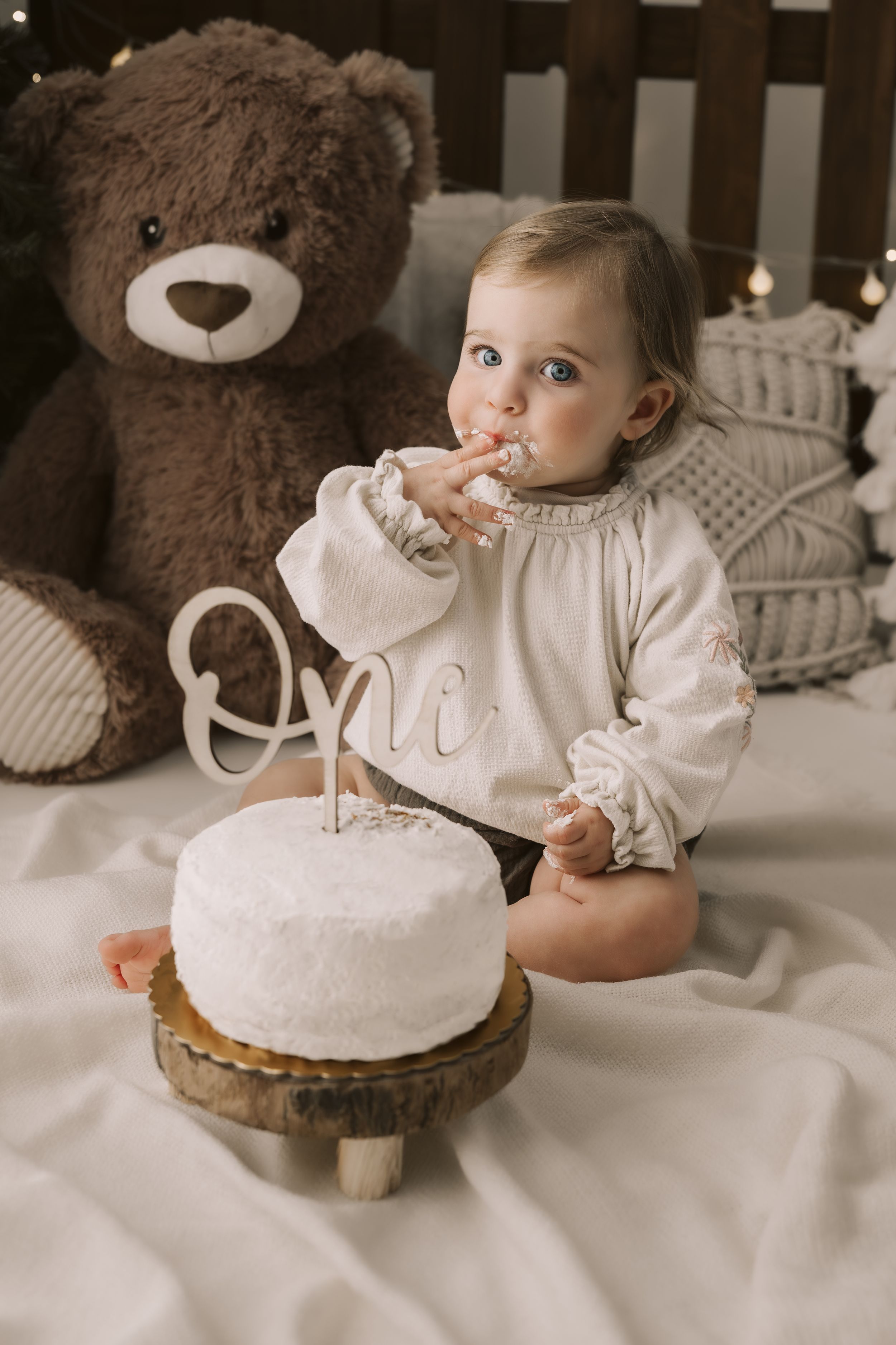 Bambina di un anno assaggia una torta con le mani sporche di panna e sullo sfondo un orso di peluches