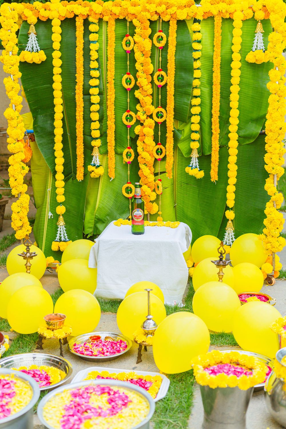 Yellow marigold garland decoration with green backdrop and flower petals for traditional ceremony.