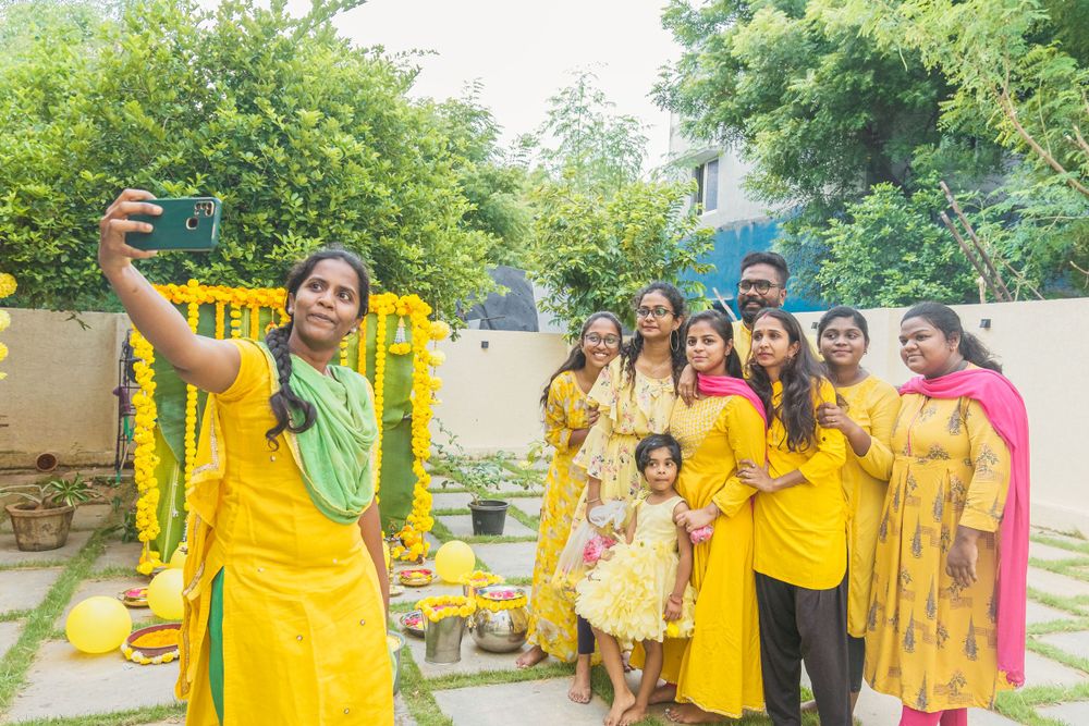 Festive gathering with group in yellow attire taking photos near floral decorations.