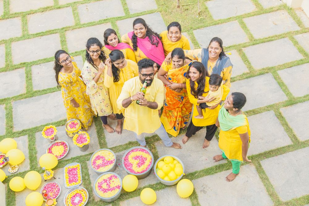 A group in yellow traditional attire poses with decorative rangoli patterns and flowers during a festive celebration.