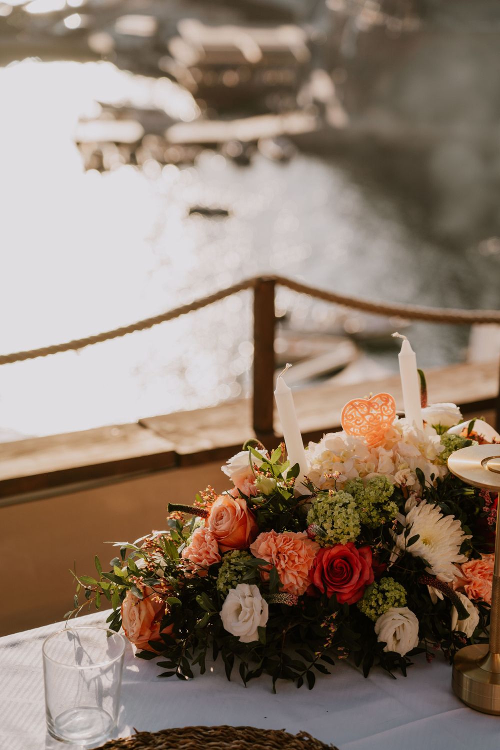 Elegant floral centerpiece with coral and white roses on a white tablecloth with mountain views.
