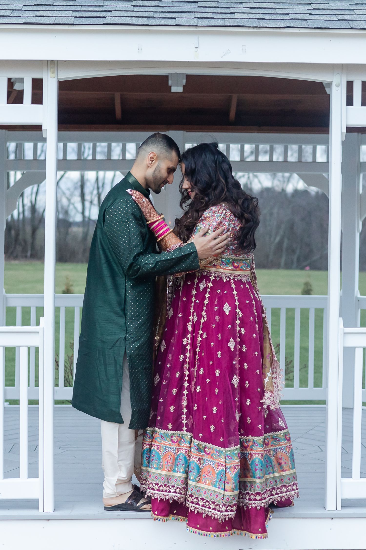 Couple in traditional South Asian wedding attire sharing an intimate moment in a gazebo.
