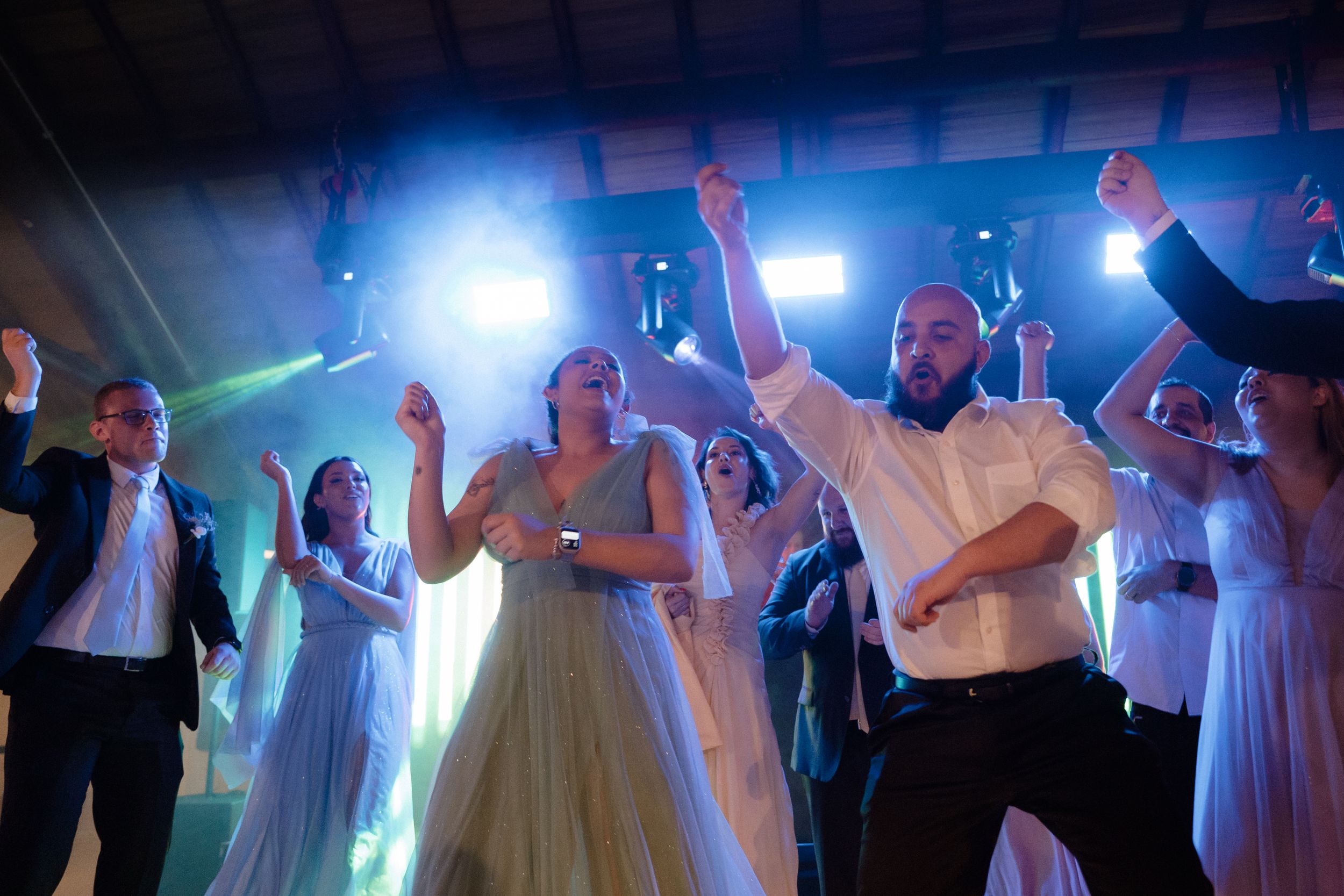 Energetic dance party with hands raised under blue and white stage lighting.