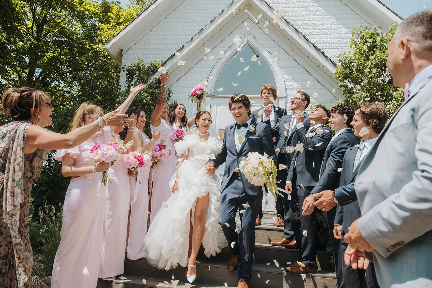 Wedding party celebrates with confetti toss on church steps during summer celebration.