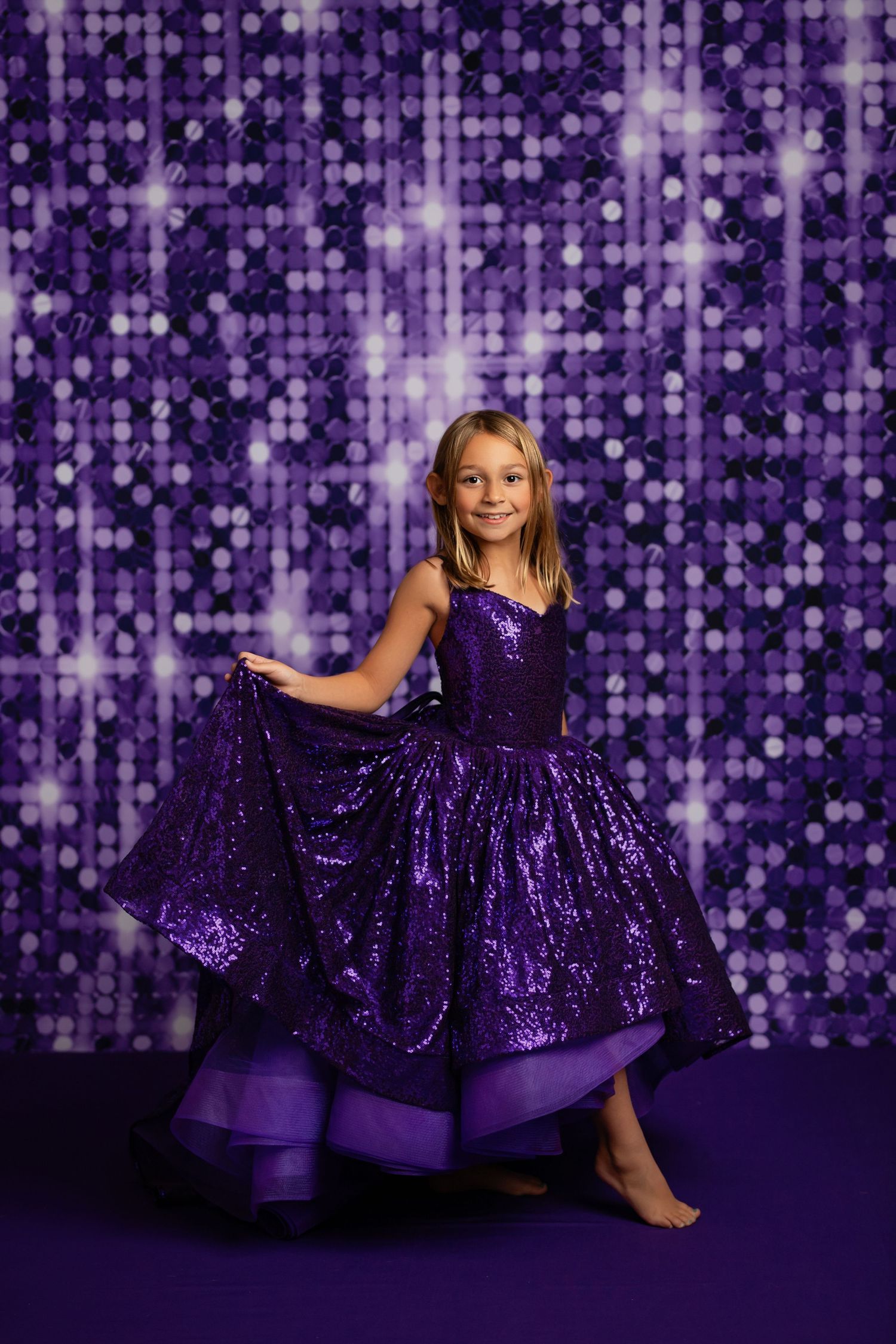Layered purple ball gown photographed against magical bokeh stage lighting.