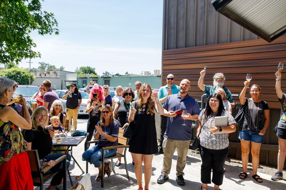 Large group of people gathered outside a building on a sunny day enjoying a casual outdoor event.