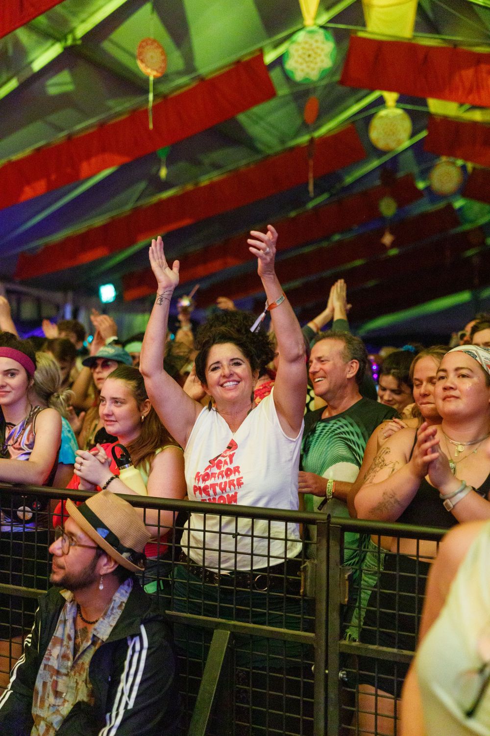 Enthusiastic crowd cheering under colorful tent at outdoor music festival.
